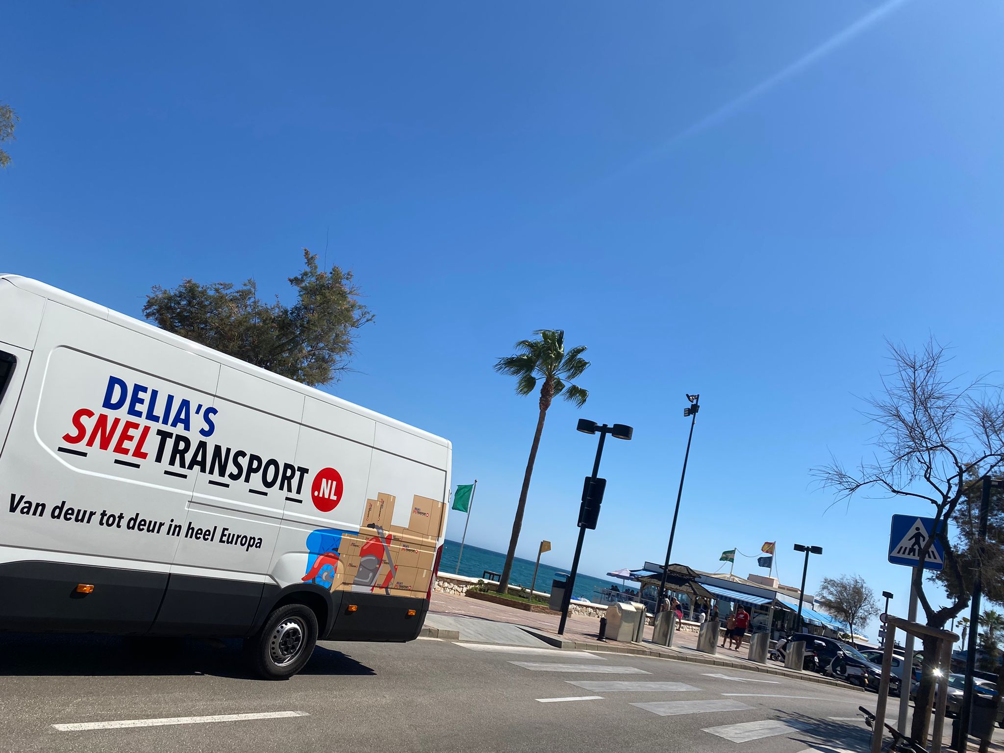 Bus van Delia's Sneltransport op een boulevard met palmbomen in Spanje